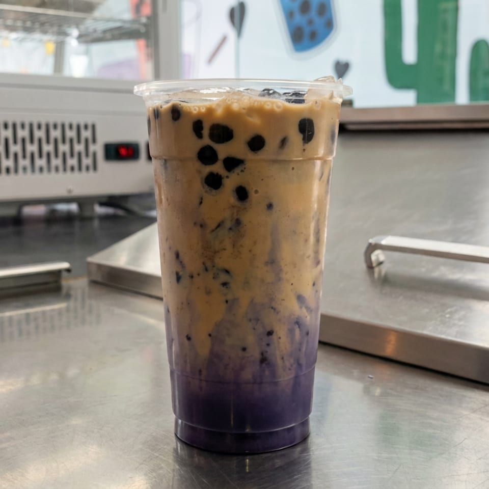 Layered purple and creamy brown bubble tea with tapioca pearls in a clear cup on a stainless-steel counter.